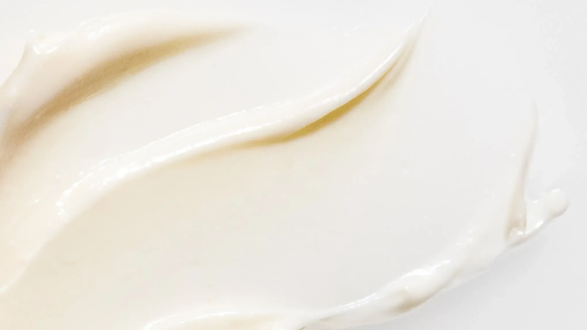 Nærbilde av en kremaktig, hvit hudpleieprodukt spredt på en hvit bakgrunn