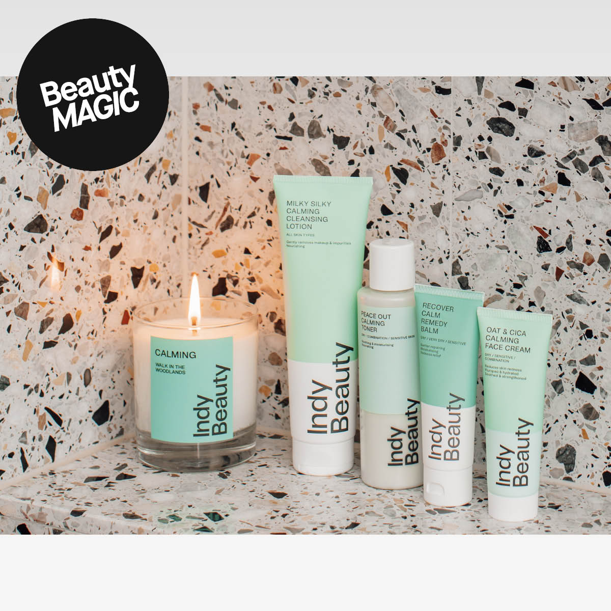 Indy Beauty-hudvårdsprodukter i gröna och vita förpackningar placerade på en stenyta tillsammans med ett tänt doftljus. I bildens övre hörn syns en svart cirkel med texten ”Beauty MAGIC”.