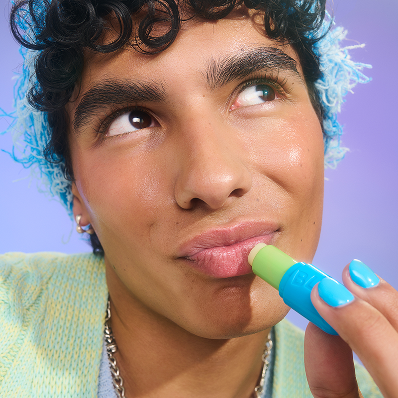 En person med blå naglar och blå hatt. Bakgrunden är lila.