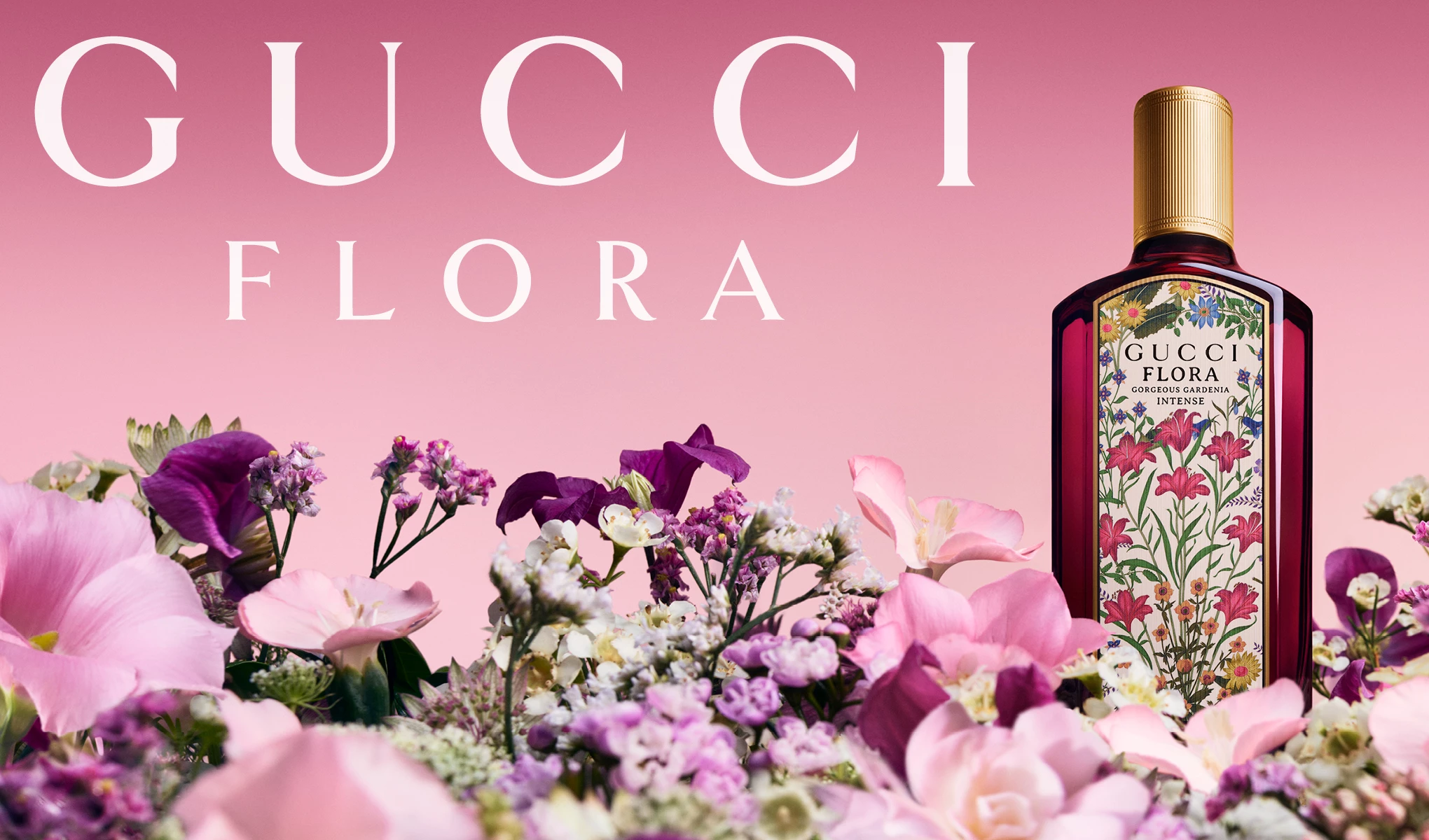 En Gucci Flora Gorgeous Gardenia parfymeflaske står blant fargerike blomster mot en rosa bakgrunn.