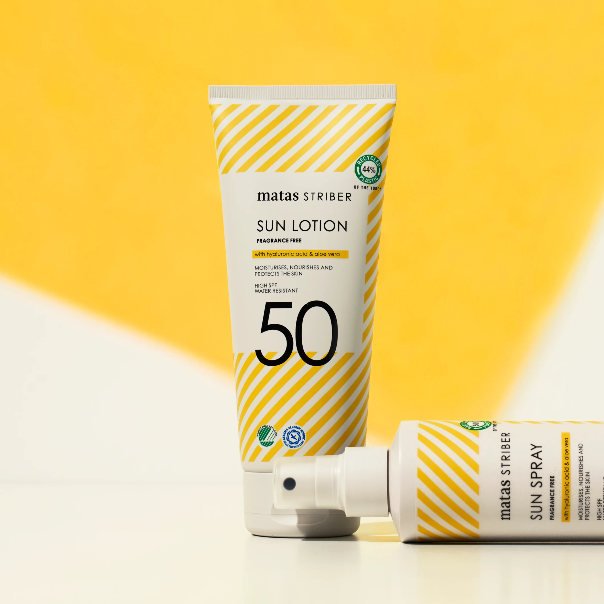 Matas Striber Sun Lotion SPF 50 -aurinkovoide pystyasennossa sekä Sun Spray -pullo vaakatasossa keltaista taustaa vasten.