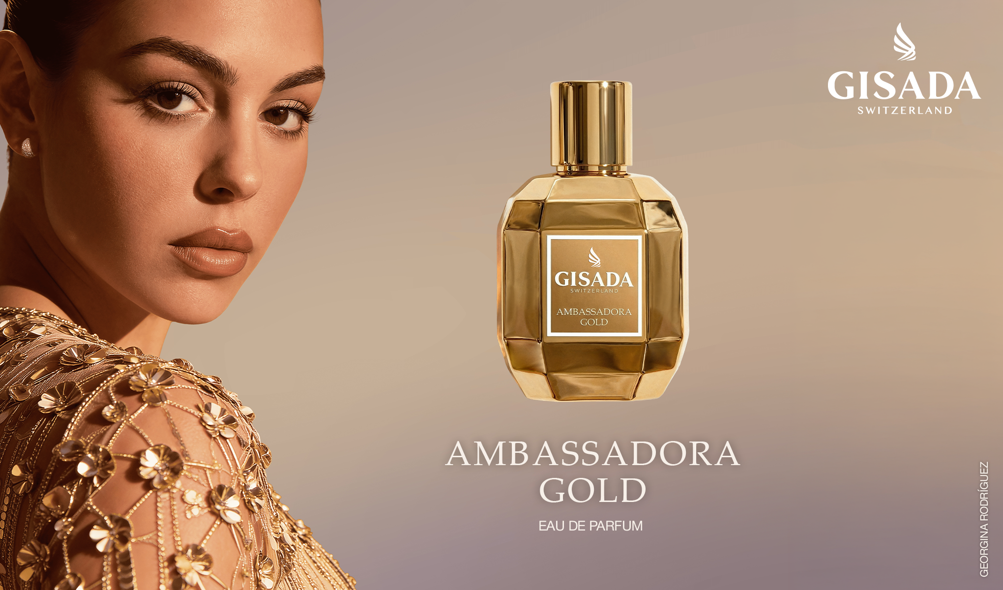 Gisada Switzerland Ambassadora Gold -hajuvesipullo kullanvärisessä designissa seisoo hohtavan kultaisella kivitasolla. Taustalla näkyy kullanvärisiä pylväitä, kalliomuodostelmia, meri ja vuoria lämpimässä valossa sekä teksti "Gisada Switzerland" ja pullon etiketti "GISADA SWITZERLAND AMBASSADORA GOLD".