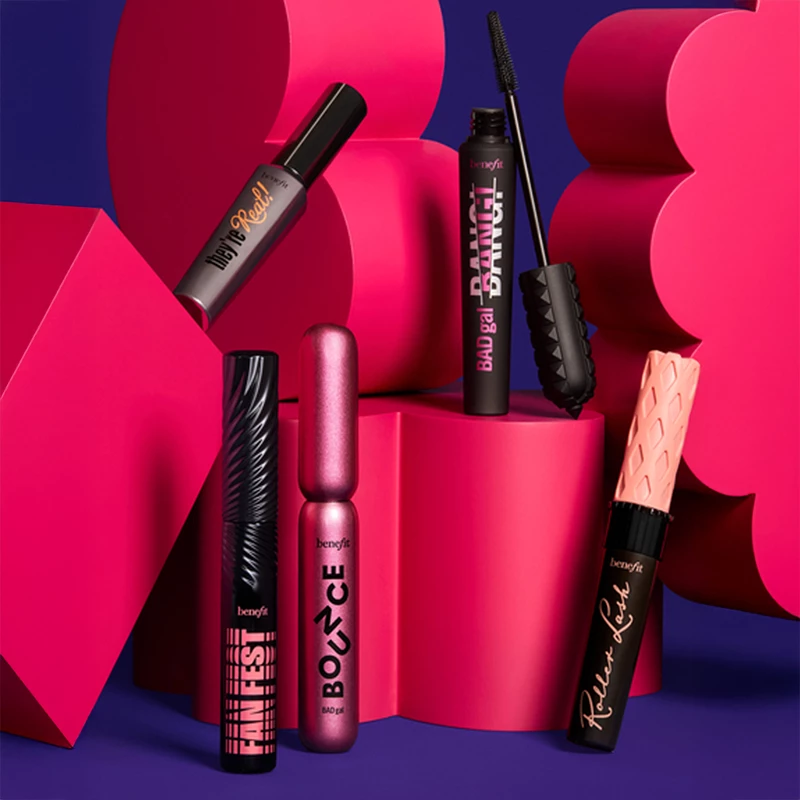 Benefit Cosmeticsin viisi erilaista ripsiväriä on esillä värikkäällä taustalla, jossa on vaaleanpunaisia ja violetteja geometrisia muotoja. Tuotteilla on ainutlaatuinen ja värikäs muotoilu.