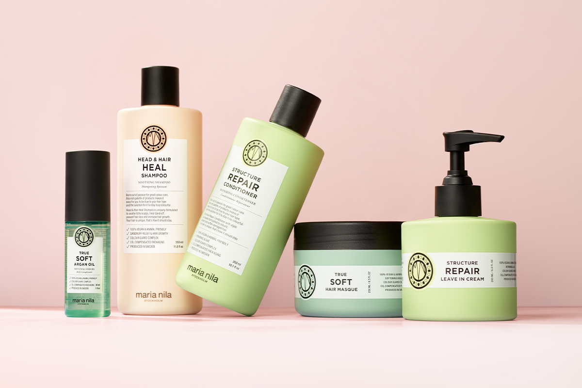 Kokoelma Maria Nilan hiustenhoitotuotteita vaaleanpunaisella taustalla. Pulloissa ja purkeissa on tyylikäs muotoilu ja eriväriset etiketit.
