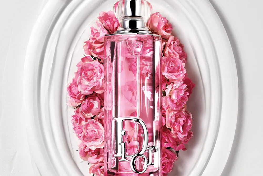 Dior Addict Lip Glow Oil i rosa flaske plassert i et dekorativt hvitt fat omgitt av rosa blomster.