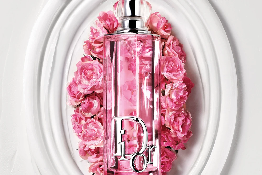 Rosa Dior Addict Lip Glow Oil -huuliöljypullo valkoisella koristeellisella vadilla vaaleanpunaisten kukkien ympäröimänä.