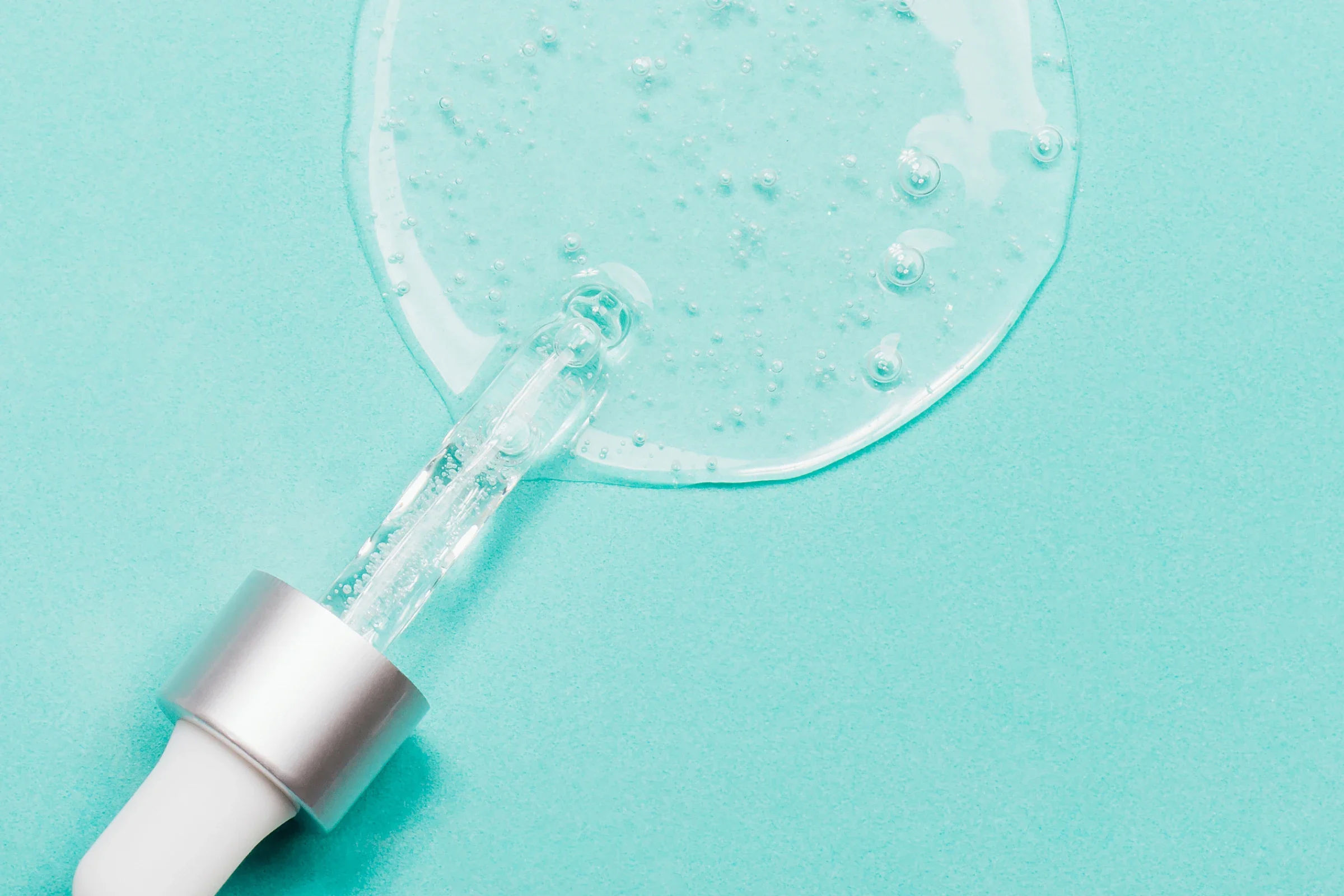 Närbild av genomskinlig gel- eller serumliknande textur med luftbubblor, fotograferad mot ljus bakgrund.