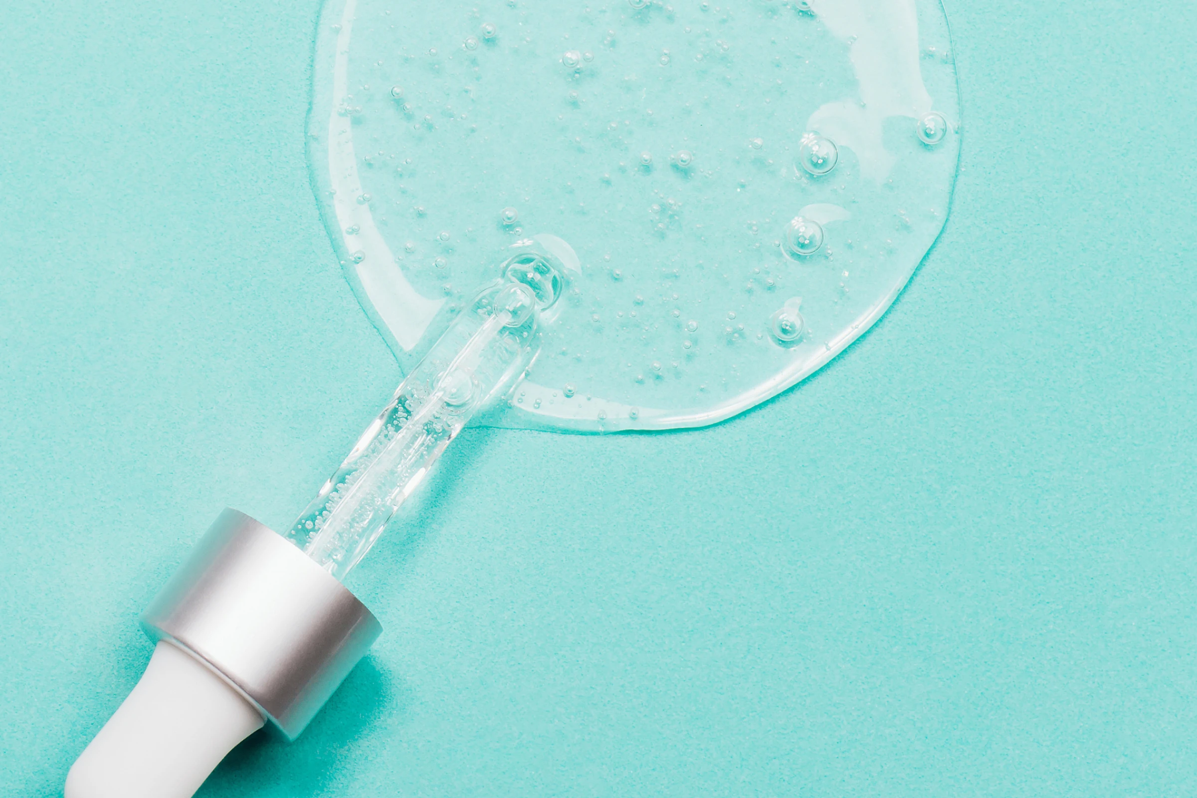 Lähikuva kirkkaasta geeli- tai seerumimaisesta koostumuksesta, jossa näkyy ilmakuplia, vaaleaa taustaa vasten.