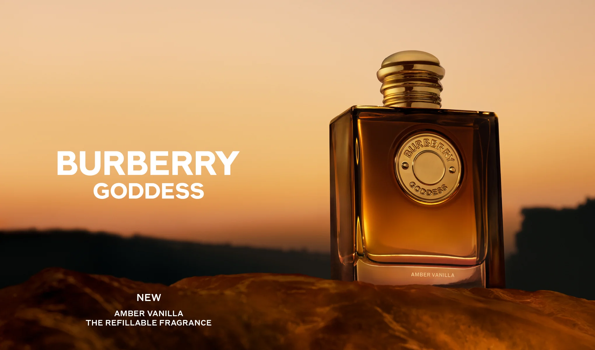 Burberry Goddess Amber Vanilla parfyme i en ravfarget flaske med gullfarget kork mot en varm oransje bakgrunn. Teksten lyder «BURBERRY GODDESS», «NEW», «AMBER VANILLA» og «THE REFILLABLE FRAGRANCE».