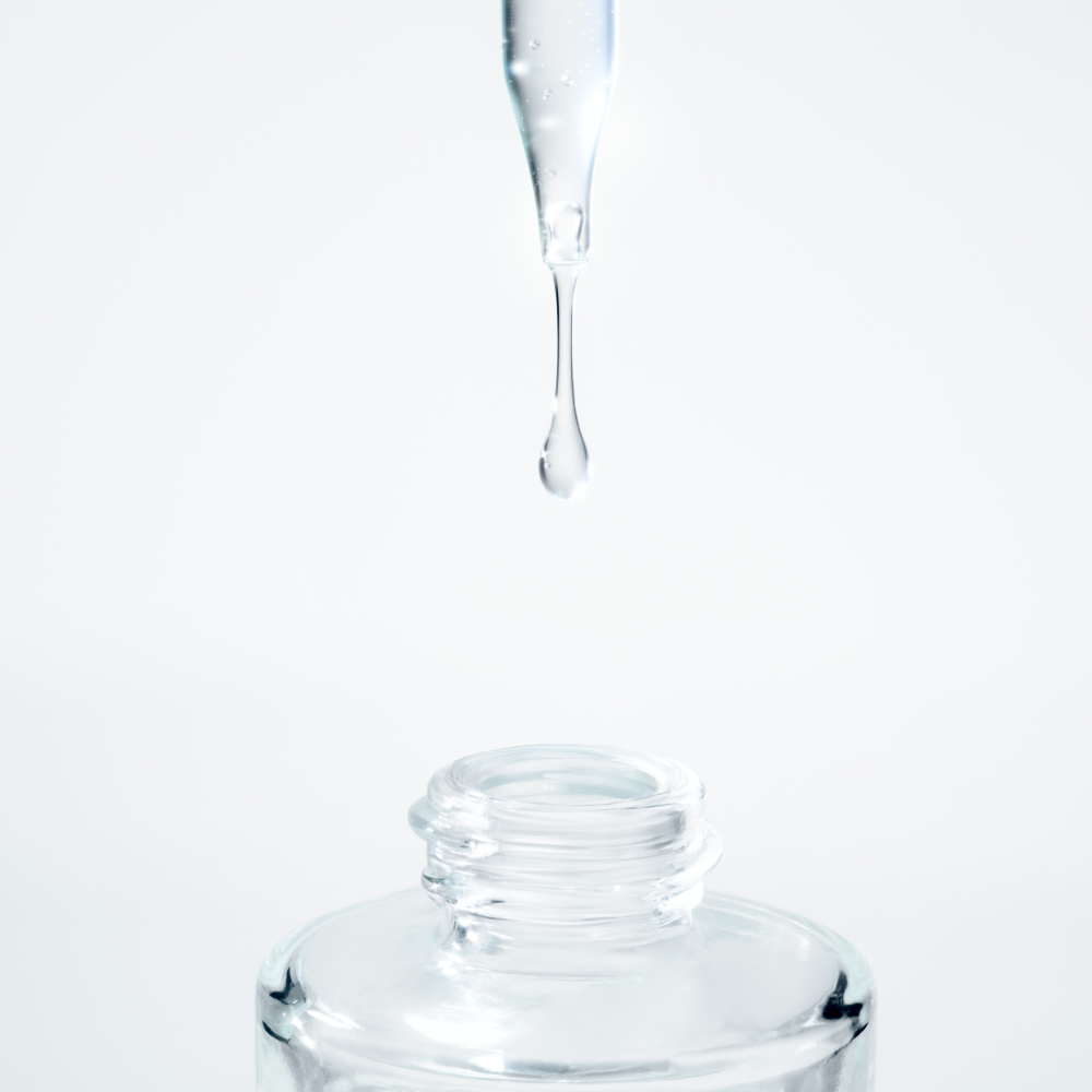 Nærbilde av en klar væske som drypper fra en pipette ned i en glassflaske.