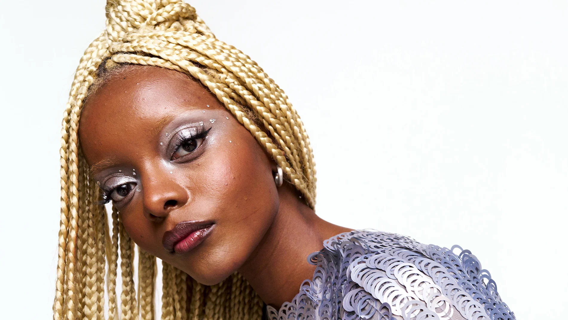 Modell med långa blonda flätor, metallic ögonskugga och grafisk eyeliner – en inspirerande festlook med fokus på glow, trendig makeup och kreativa beauty hacks.