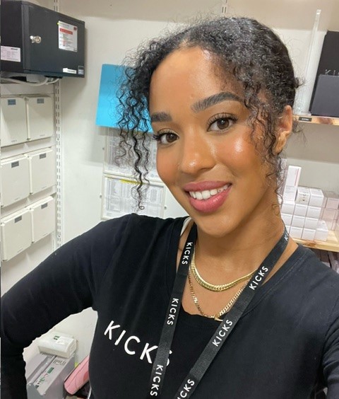 Person med svart, lockigt hår och makeup som ler till kameran
