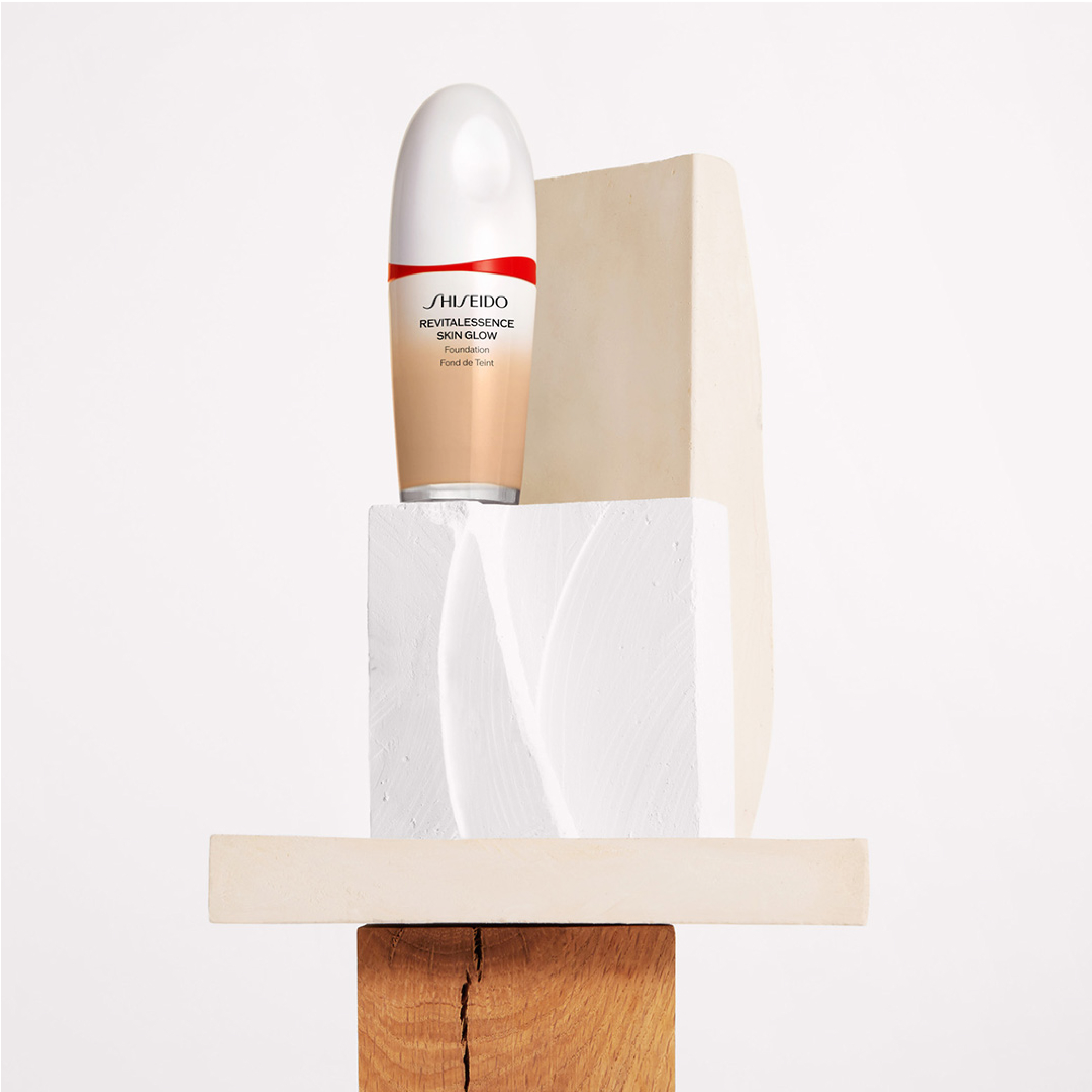 Ett Shiseido-serum i en vit och beige flaska, placerad på en vit piedestal med en beige bakgrund.
