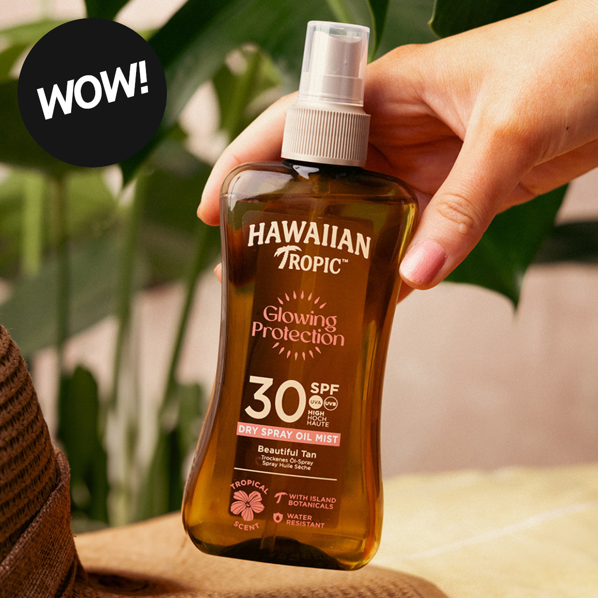 Käsi pitää ruskeaa Hawaiian Tropic “Glowing Protection” SPF 30 “Dry Spray Oil Mist” -suihketta, jossa tekstit “Beautiful Tan”, “Tropical Scent” ja “Water Resistant”.