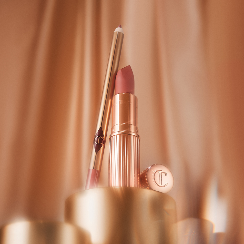 En läppstift och en läppenna i roséguld står elegant mot gyllene bakgrundselement. Bakgrunden har en mjuk ton som skapar en lyxig atmosfär.