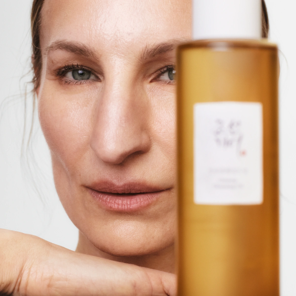 Nærbilde av ansikt ved siden av en hudpleieflaske i brun transparent flaske.