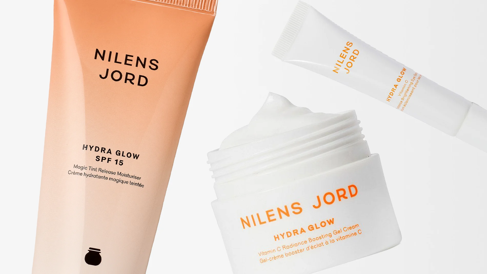 Tre hudvårdsprodukter från Nilens Jord ur serien Hydra Glow visas mot en ljus bakgrund. Bilden inkluderar en fuktgivande dagkräm med SPF 15, en gelkräm i burk och en ögonkräm. Produkterna har en beige till vit design och förmedlar en känsla av återfuktning, lyster och naturlig skönhet.