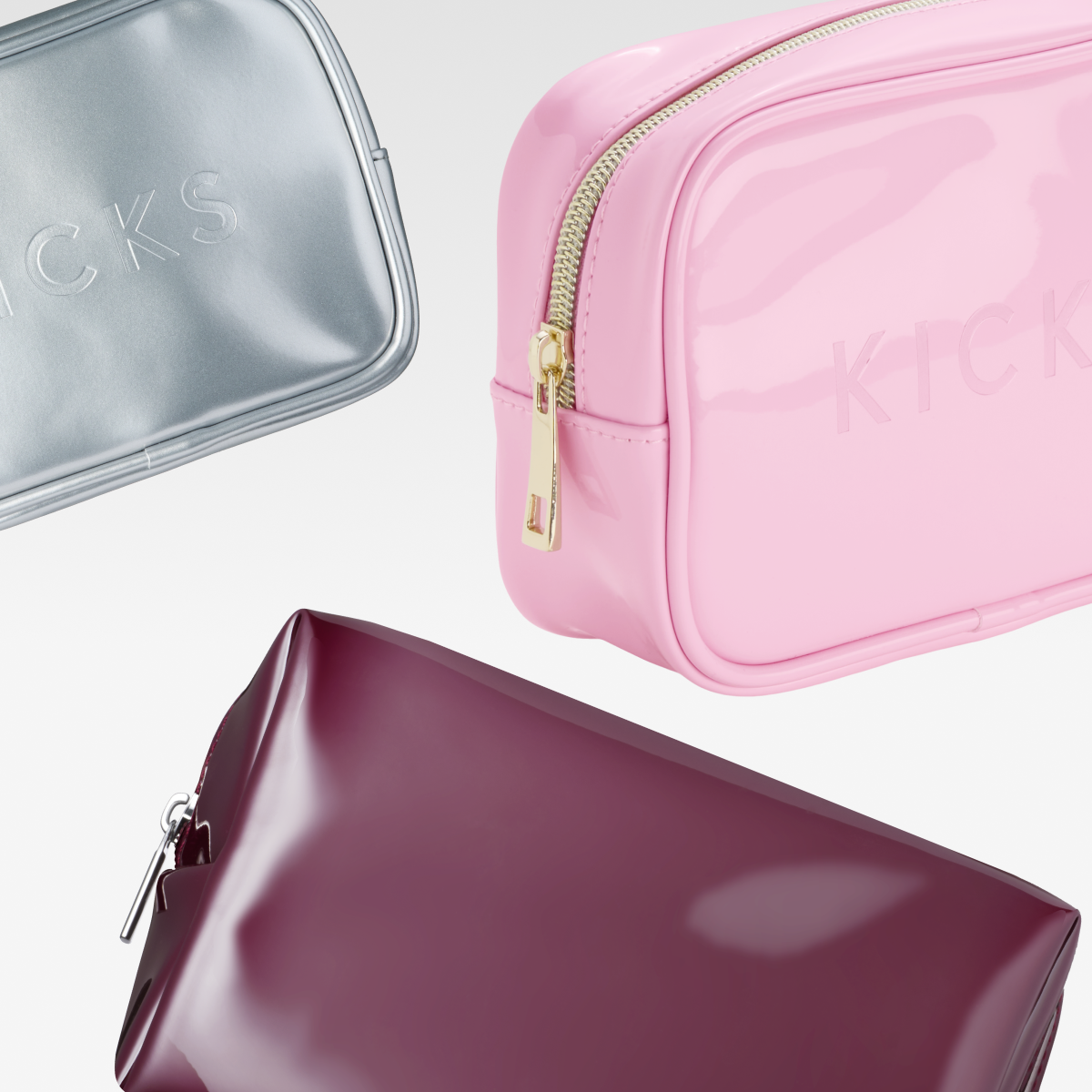 Tre sminkväskor i olika färger mot vit bakgrund: silver, rosa och vinröd.