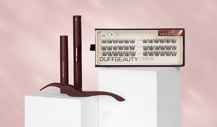 DuffBeauty-vippekluster og to vippeforlengelsesprodukter mot en rosa bakgrunn. På den hvite sokkelen er det også et brunt verktøy for vippeforlengelse.