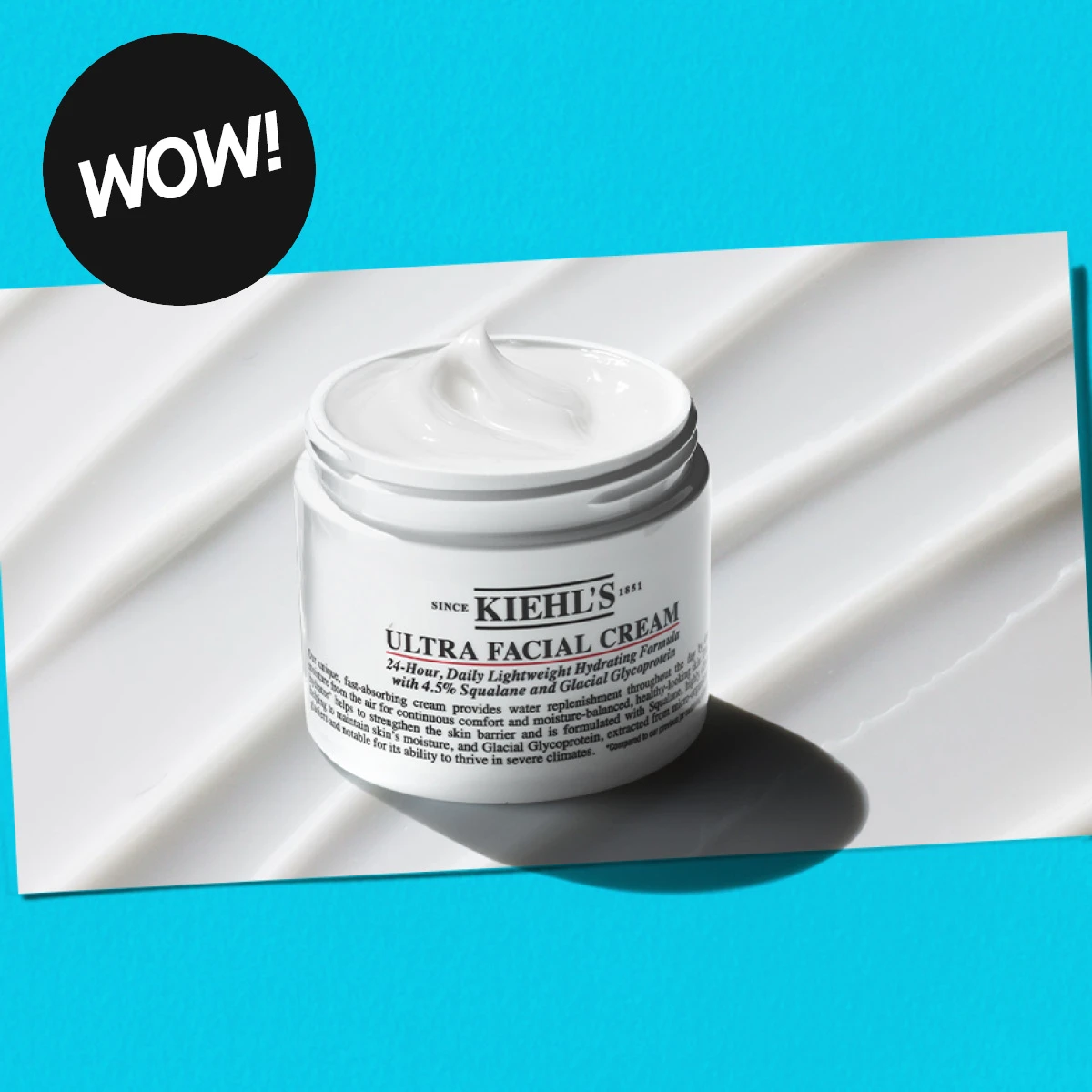 Krukke med Kiehl's Ultra Facial Cream på en hvit, bølgete overflate. Teksten 'WOW!' i svart sirkel.