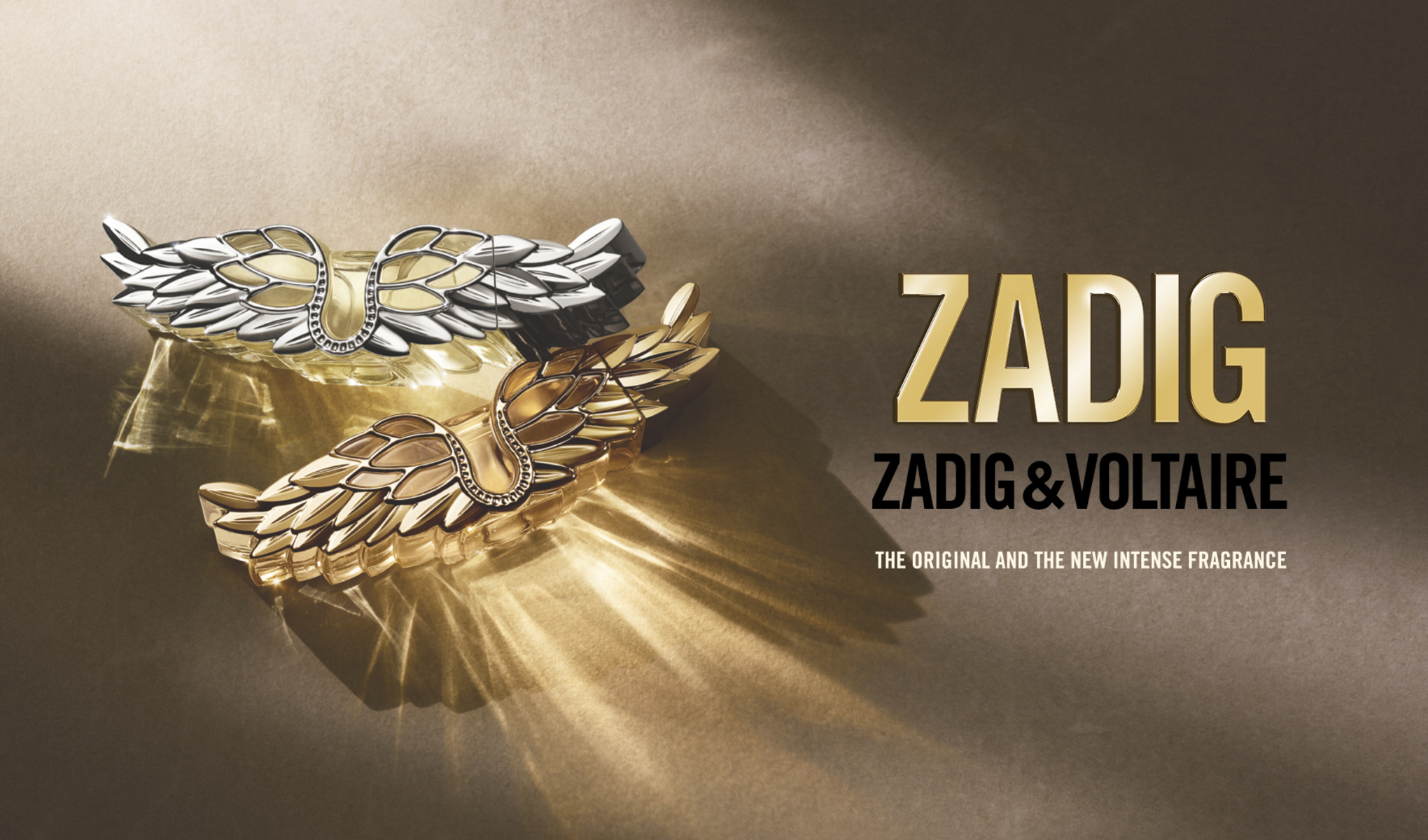 Nærbilde av Zadig & Voltaire Zadig-parfymer formet som vinger i gull og sølv, med teksten «The Original and the New Intense Fragrance».