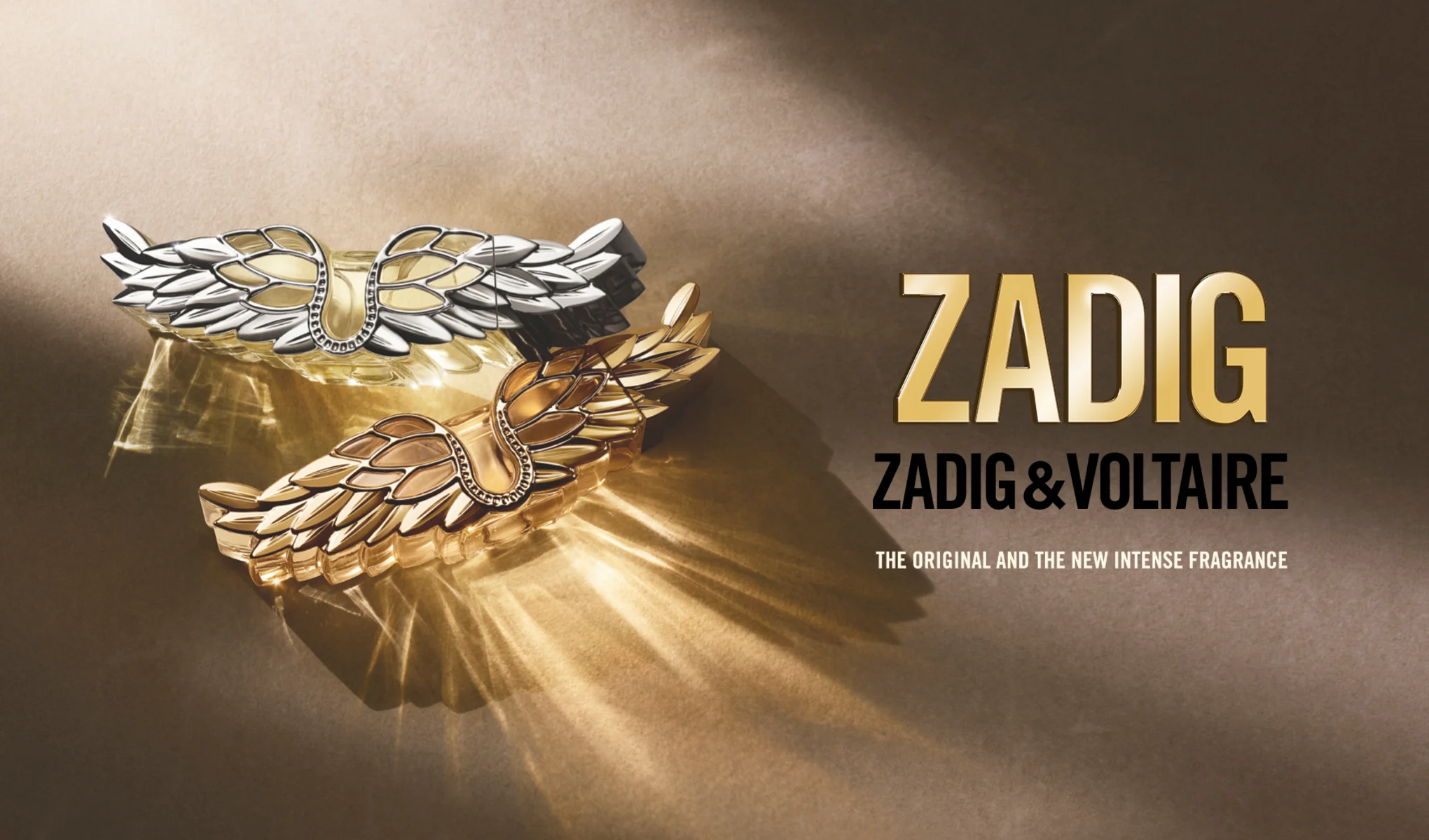 Nærbilde av Zadig & Voltaire Zadig-parfymer formet som vinger i gull og sølv, med teksten «The Original and the New Intense Fragrance».