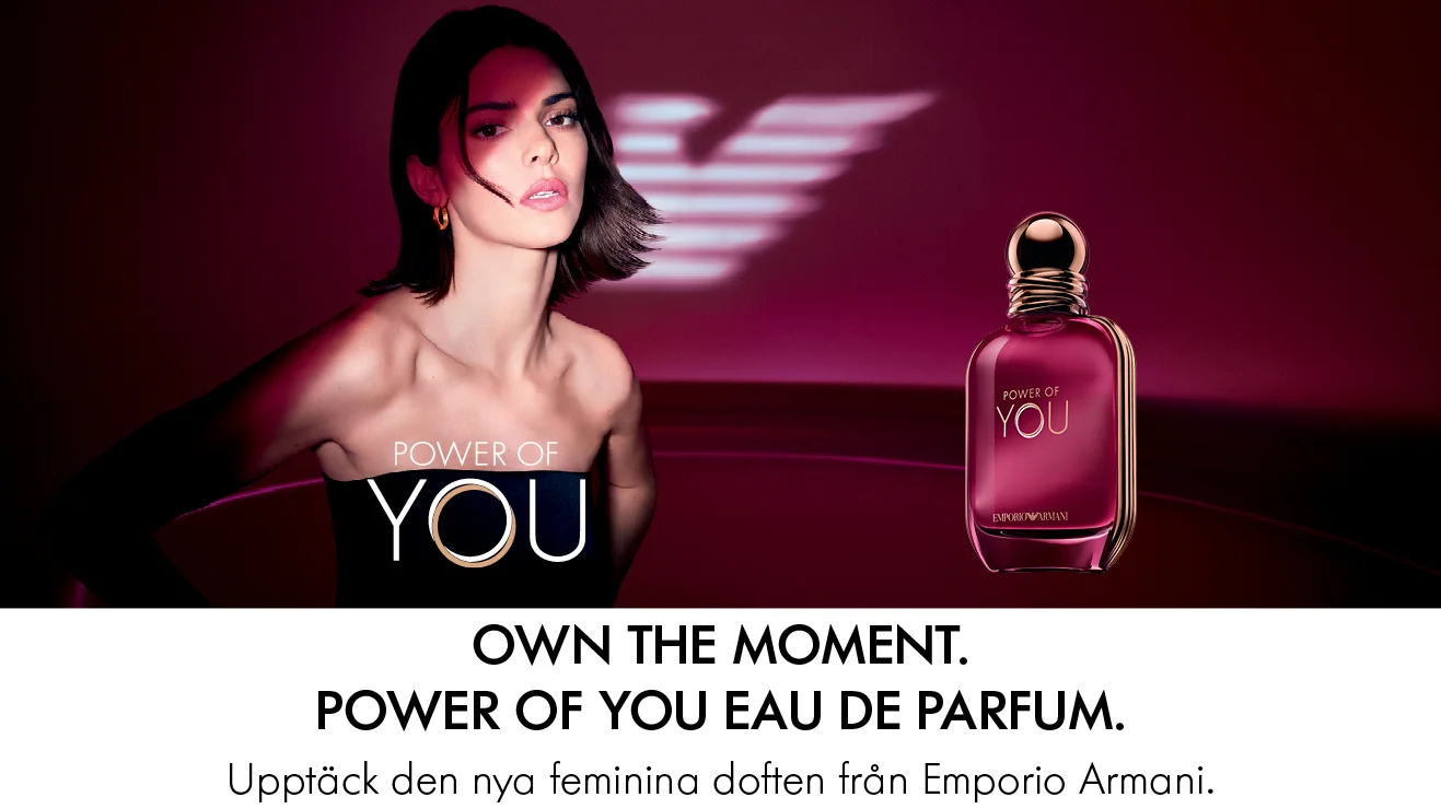 En elegant kvinna i djupt röd belysning möter blicken, med en rosa Power of You-parfymflaska med guldkork bredvid. Känslan är modern och självsäker.