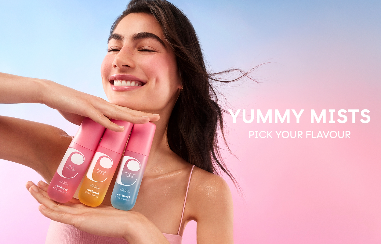 Leende person håller tre Cacharel Yummy Mists body mists mot rosa och blå bakgrund. Bilden innehåller texterna ”Yummy Mists” och ”Pick Your Flavour”.
