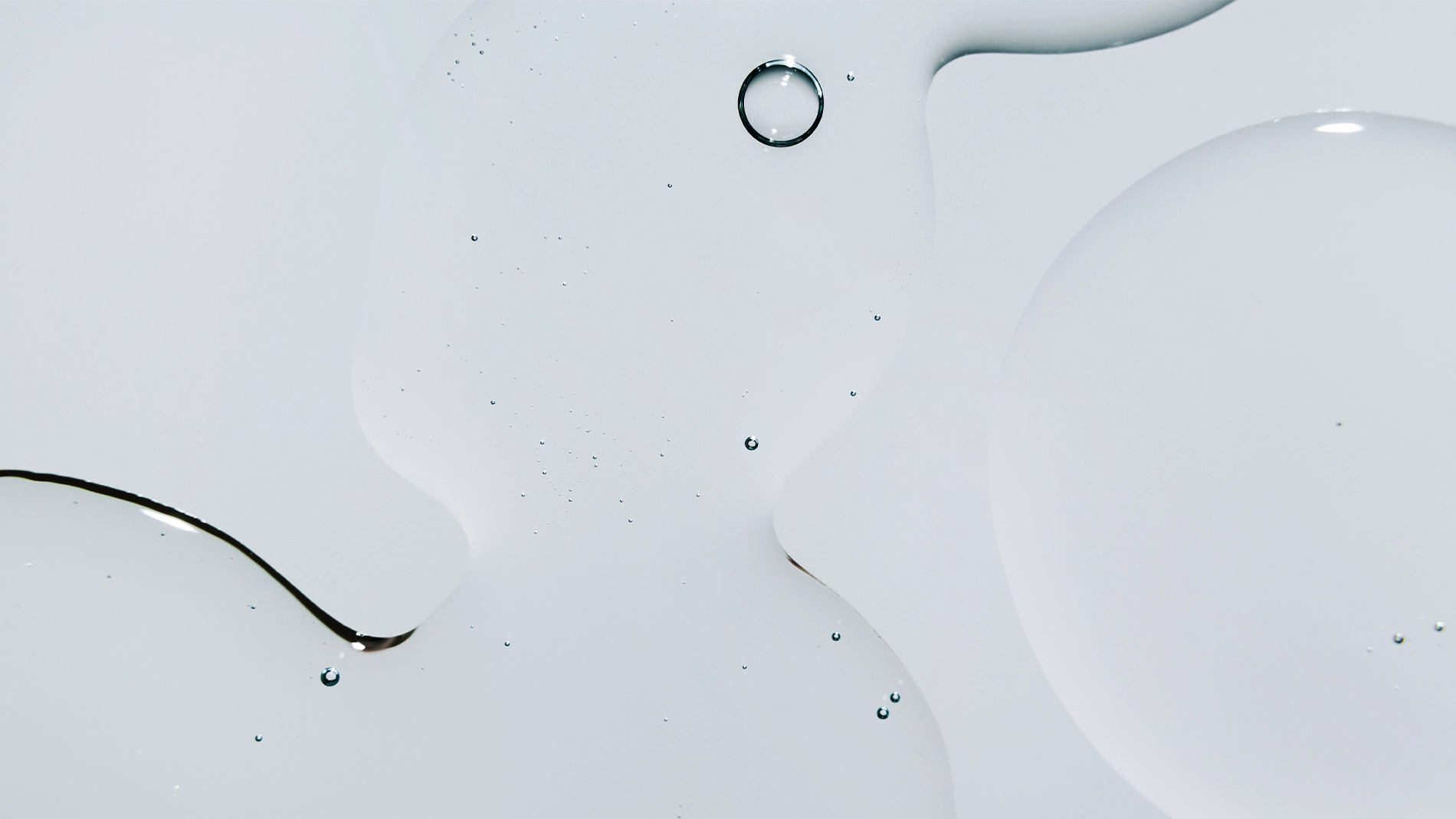 Nærbilde av klare væskedråper i ulike former på hvit overflate med myke refleksjoner.