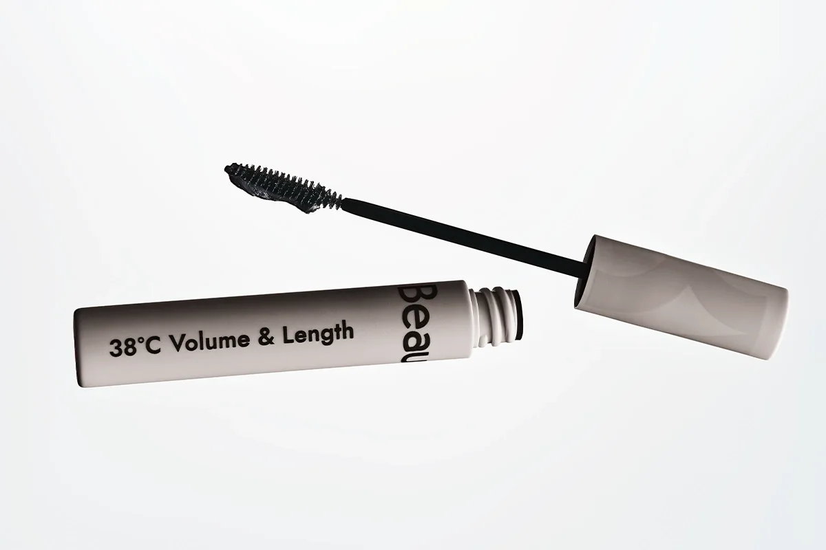 Avattu mascara, jossa on musta ripsiväriharja ja vaalea pakkaus valkoista taustaa vasten. Pakkauksessa lukee ”38°C Volume & Length” ja ”Beau”.