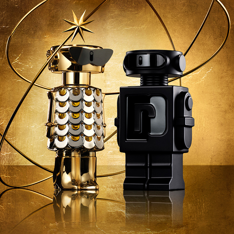 Kaksi robotin muotoista hajuvesipulloa, toinen kultainen ja toinen musta, seisoo kultaisella taustalla. Pullon ympärillä on tähti ja pyöreitä linjoja.