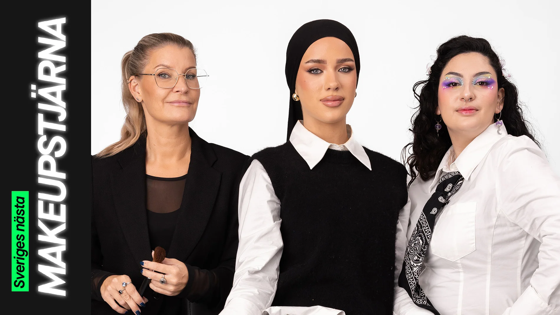 Tre personer sitter tillsammans, där en håller en makeupborste och de andra bär kreativa makeuplooker – en med markerad bas och eyeliner samt en med färgstark ögonmakeup med glitterdetaljer.