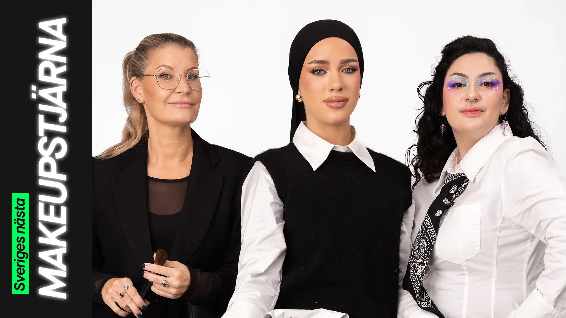 Tre personer sitter tillsammans, där en håller en makeupborste och de andra bär kreativa makeuplooker – en med markerad bas och eyeliner samt en med färgstark ögonmakeup med glitterdetaljer.