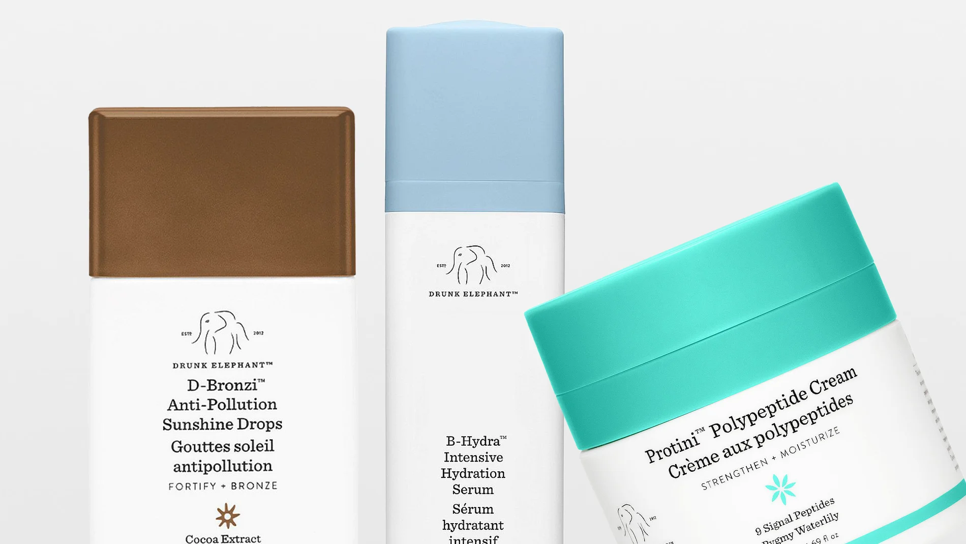Tre hudpleieprodukter fra Drunk Elephant vises mot lys bakgrunn: D-Bronzi Anti-Pollution Sunshine Drops i brun flaske, E-Hydra Intensive Hydration Serum i hvit og blå emballasje og Protini Polypeptide Cream i en krukke med turkist lokk.
