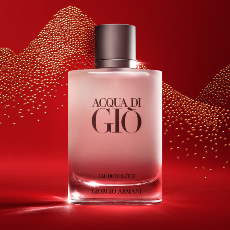 Hajuvesipullo, jossa teksti ”ACQUA DI GIÒ Eau de Toilette GIORGIO ARMANI”. Pullo on himmeä ja siinä on tumma korkki. Tausta on punainen, ja siinä on kultaisia pisteitä, jotka muodostavat aaltokuvion.