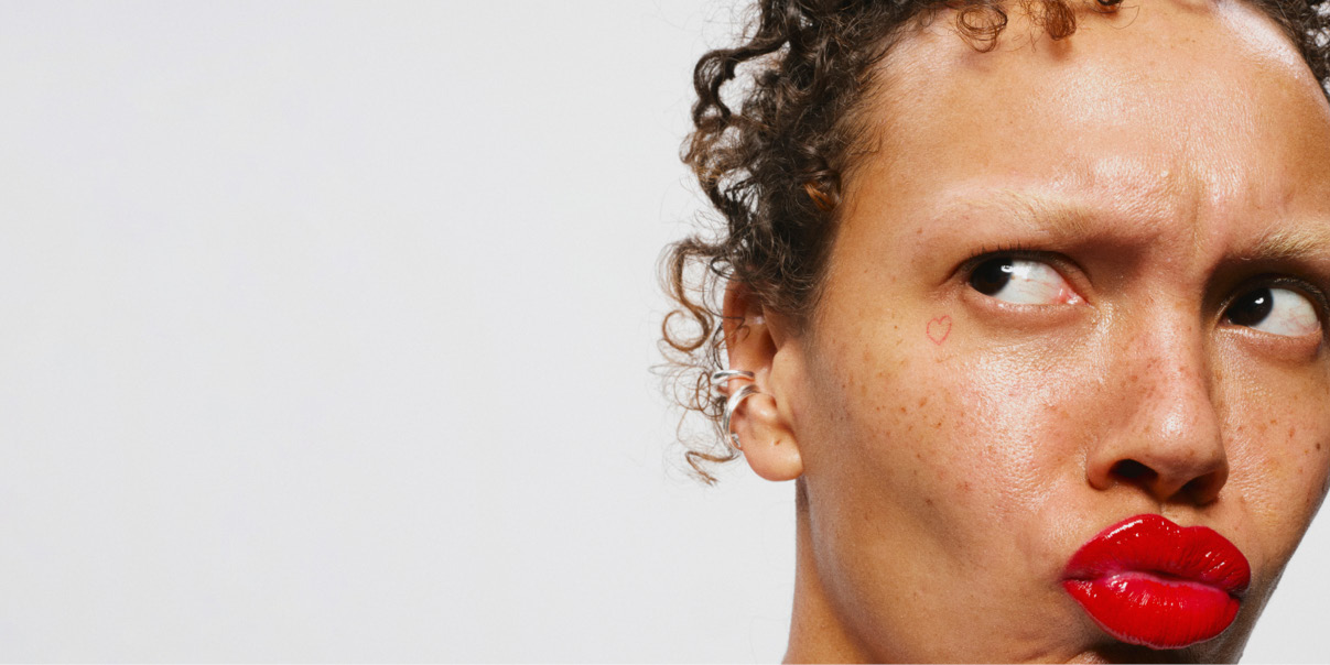 Henkilö, jolla on kiharat hiukset ja hopeinen korvakoru.