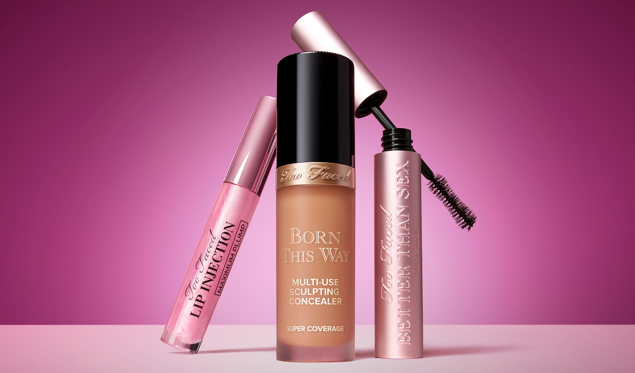 Tre kosmetikprodukter mot en rosa bakgrund. Till vänster "Too Faced Lip Injection Maximum Plump" -läppglans, i mitten "Born This Way Multi-Use Sculpting Concealer" -concealer och till höger "Better Than Sex" -mascara.
