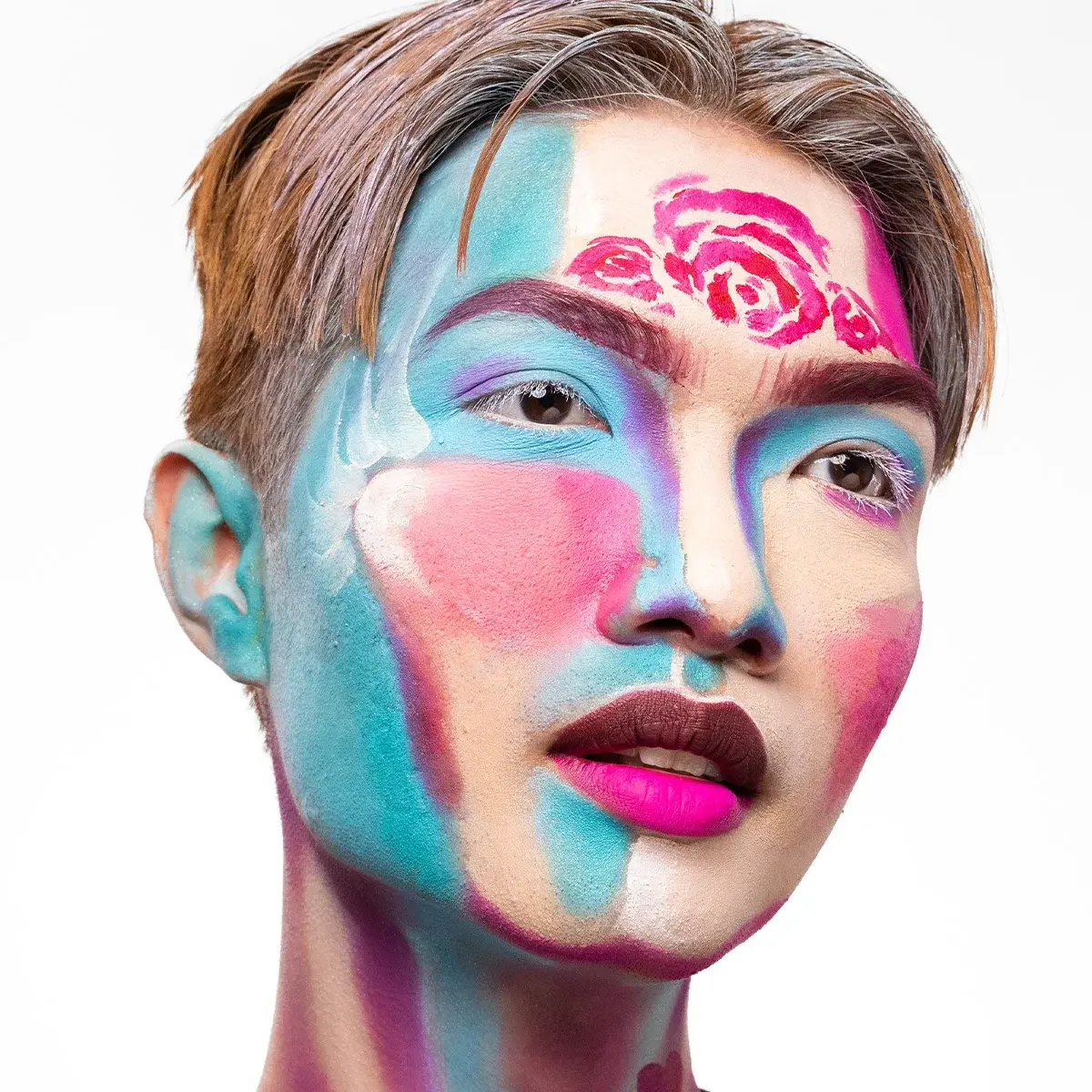 Närbild av kreativ ansiktsmålning i blå, rosa, lila och beige toner, med målade rosor i pannan, markerade bryn och tvåfärgade läppar som skapar ett konstnärligt helhetsintryck.