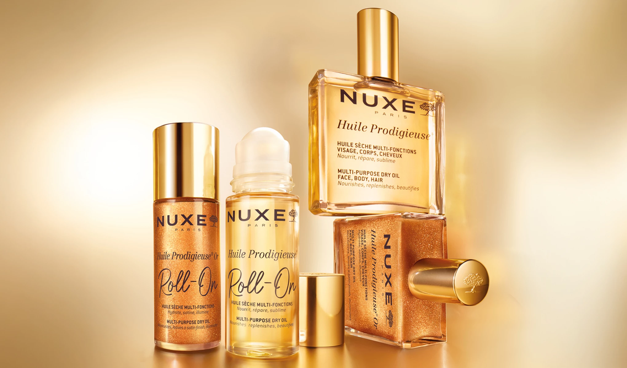 Nuxe-tuotteet, mukaan lukien Huile Prodigieuse ja Roll-On, on aseteltu tyylikkäästi kultaisen taustan eteen. Pulloissa on ylellinen muotoilu kultaisilla yksityiskohdilla.