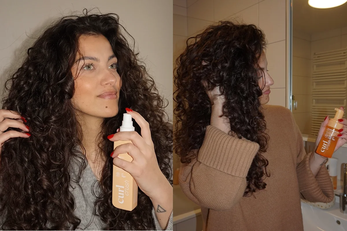Person med långt lockigt hår håller en Hairlust Curl Crush-produkt med pump och sprayar produkten mot håret. Förpackningen är beige med synlig text “curl crush”, och fokus ligger på hårvård för definierade lockar.