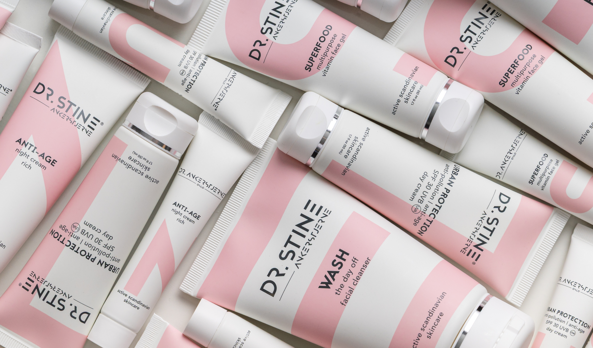 DR. STINE -ihonhoitotuotteita valkoisissa ja vaaleanpunaisissa pakkauksissa vaaleaa taustaa vasten. Näkyvä teksti sisältää “DR. STINE”, “SUPERFOOD multipurpose vitamin face gel”, “ANTI-AGE night cream rich”, “URBAN PROTECTION anti-pollution anti-age SPF 30 UVB/UVA day cream” ja “WASH the day off facial cleanser”.