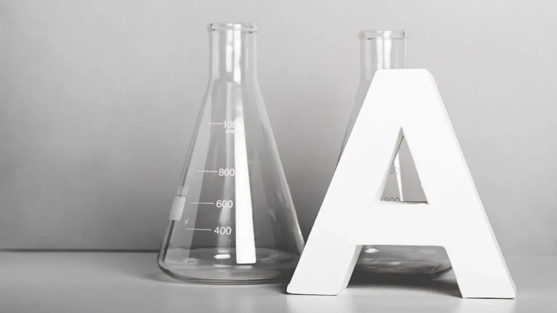 Iso A-kirjain kahden Erlenmeyer-pullon vieressä harmaalla alustalla ja taustalla.