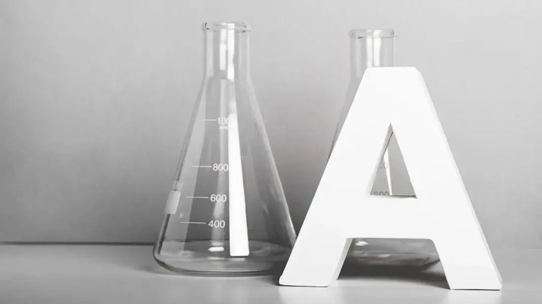 Iso A-kirjain kahden Erlenmeyer-pullon vieressä harmaalla alustalla ja taustalla.