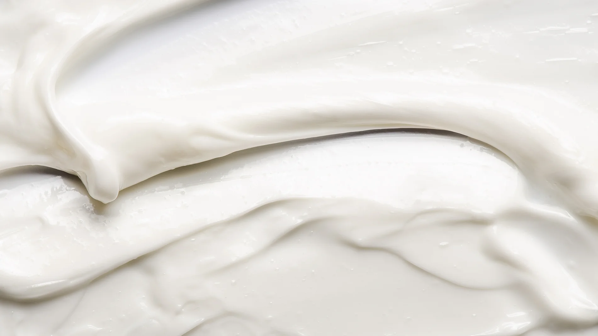 Nærbilde av hvit krem med myk, glatt og fyldig tekstur som er smurt ut i lag mot lys bakgrunn.