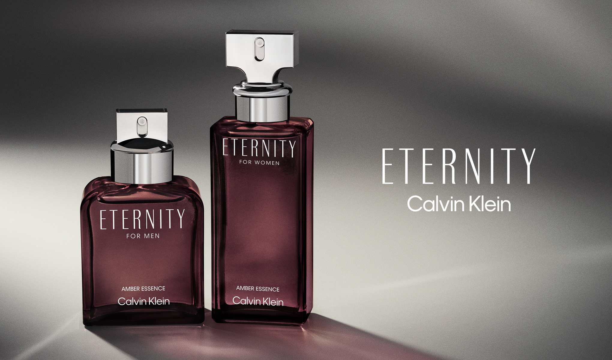 To parfymeflasker fra Calvin Klein med navnet "Eternity" for menn og kvinner. Flaskene er plassert på en grå overflate med en gradient bakgrunn. Teksten "Eternity Calvin Klein" er plassert til høyre for flaskene.