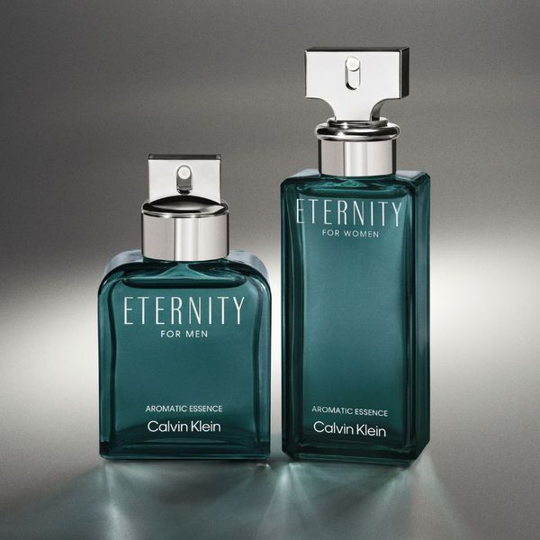Kaksi Calvin Kleinin hajuvettä nimeltä ”Eternity” miehille ja naisille. Pullot ovat tummanvihreitä, niissä on hopeanväriset korkit ja etiketissä teksti ”Aromatic Essence”. Ne on sijoitettu pinnalle, jossa on harmaa kaltevuusasteinen tausta.