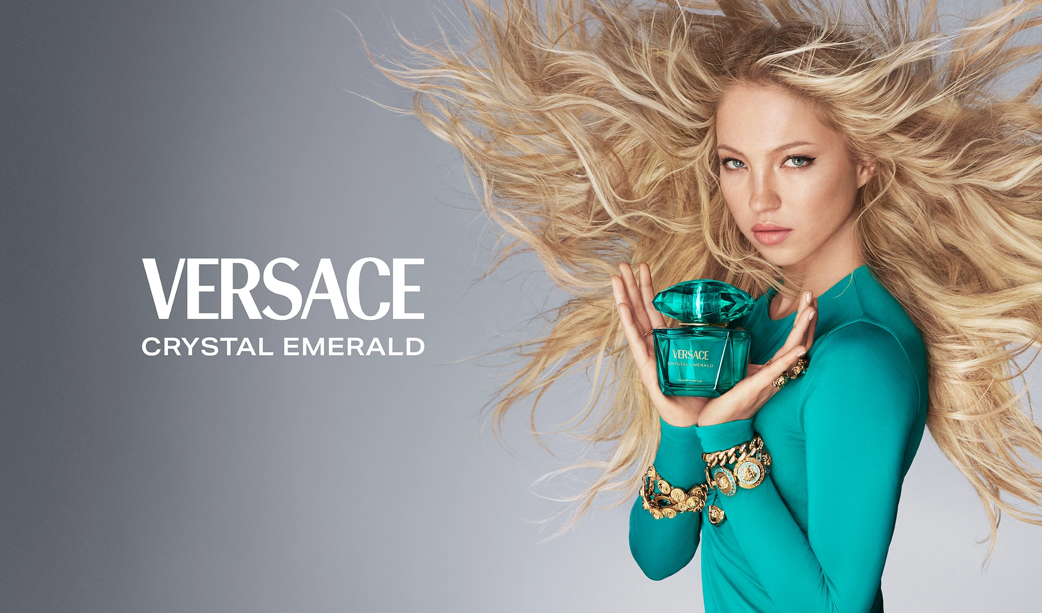 Kvinna håller Versace Crystal Emerald-parfym mot grå bakgrund.