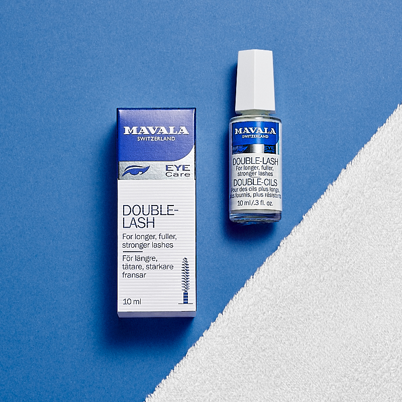 En bild på en förpackning och en flaska med Mavala Double-Lash placerade på en vit handduk med en blå bakgrund.