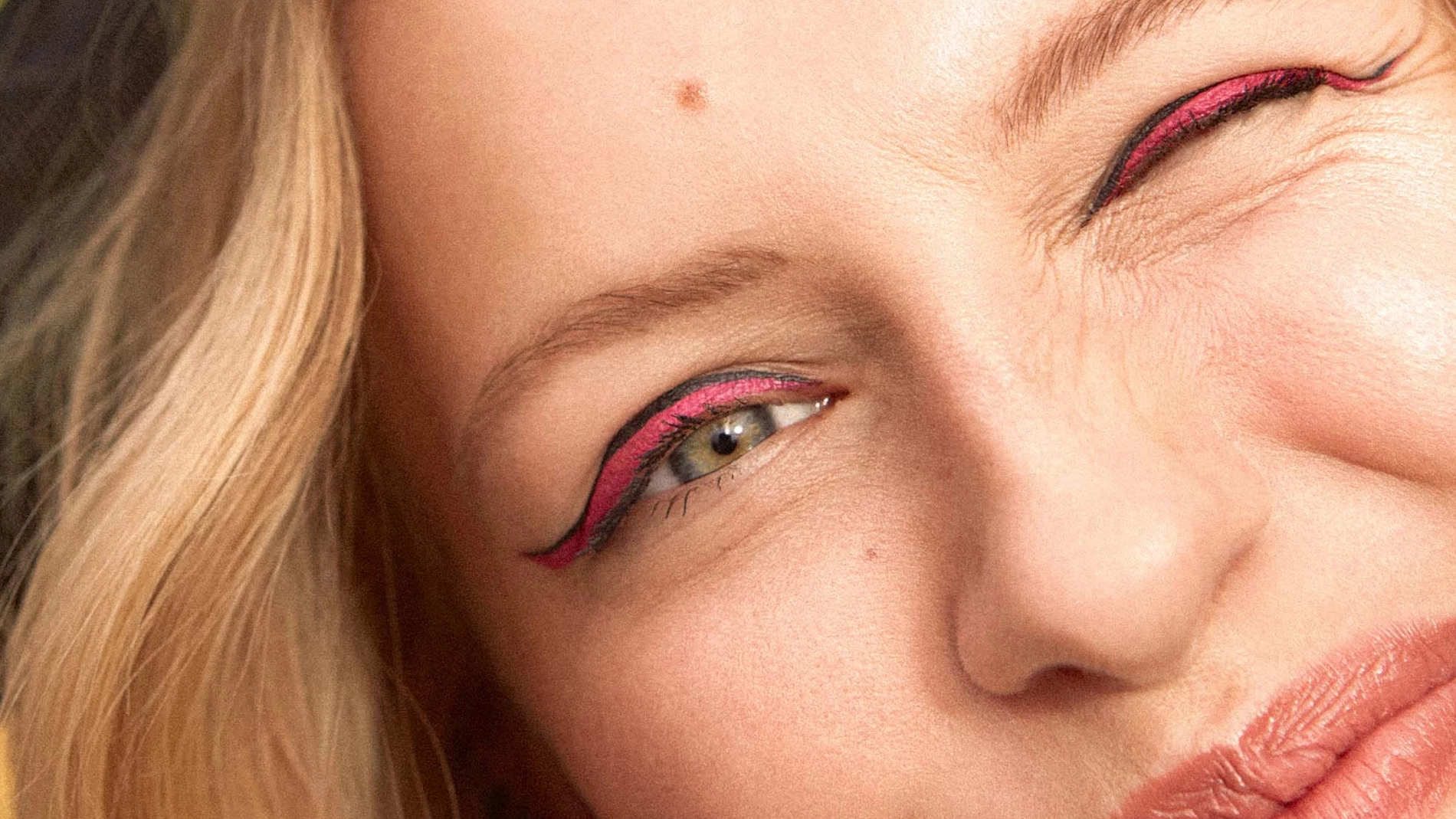 Nainen, jolla on vaaleat hiukset ja eyeliner, katsoo kameraan ja vilkuttaa yhdellä silmällä.