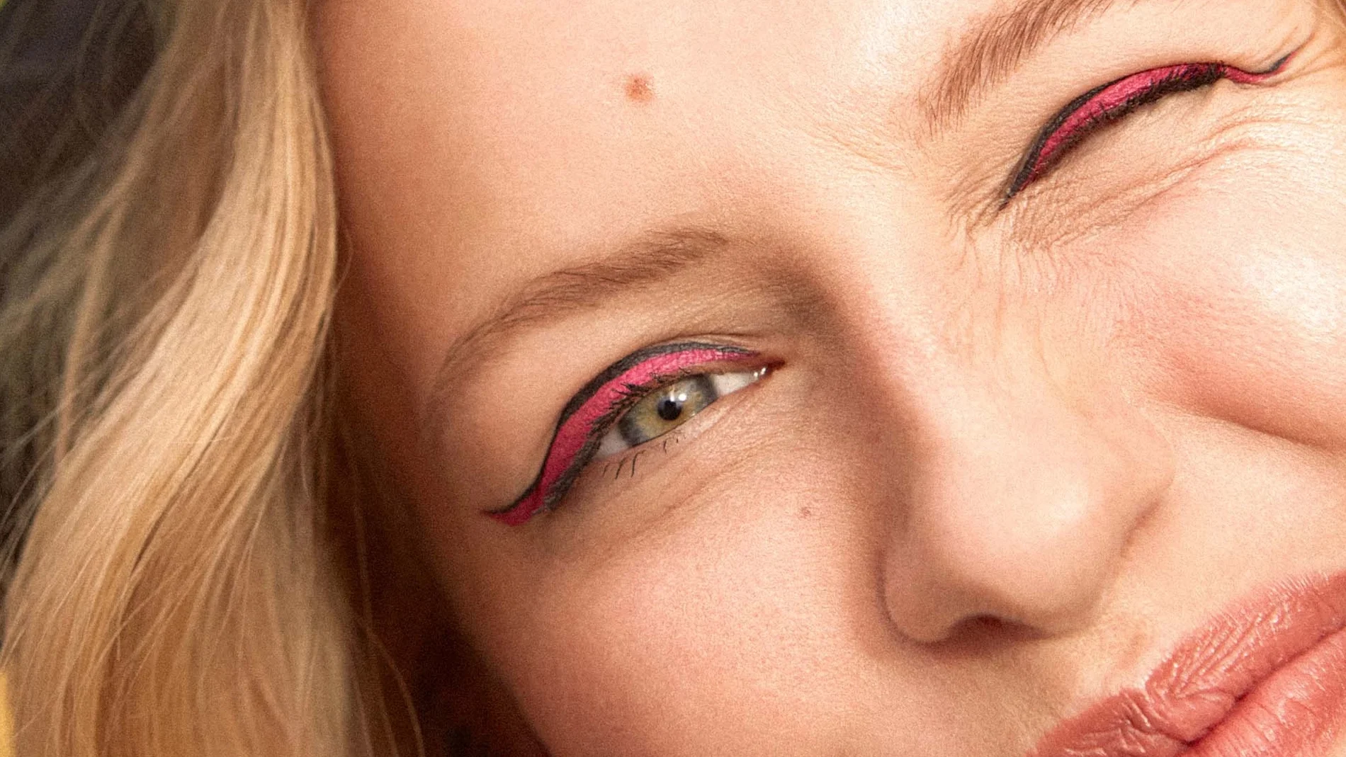 Kvinna med blondt hår och eyeliner som tittar in i kameran och blinkar med ena ögat